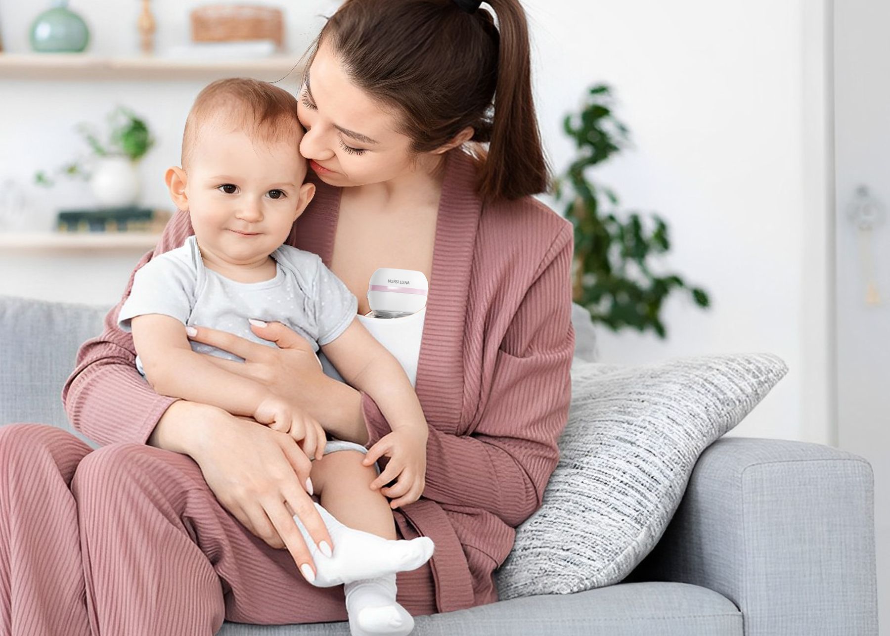 Mother holding her baby on the sofa while wearing a Nursi Luna hands-free breast pump
